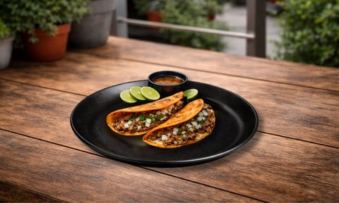 Black plate with two stuffed poblano peppers and sliced cucumber on wooden table in outdoor garden setting