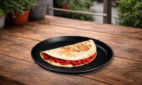 A folded crepe with red jam filling on a black plate, placed on a wooden outdoor table with potted plants in the background