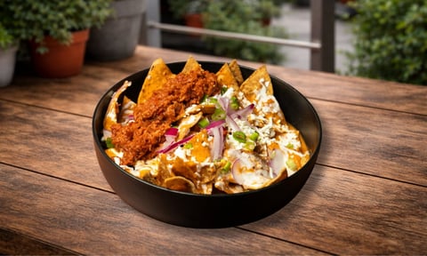 Bowl of nachos with melted cheese, crispy tortilla chips, and fresh purple onion garnish on outdoor wooden table