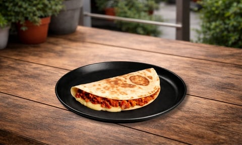 Folded quesadilla with cheese and red filling on a black plate on a wooden table outdoors