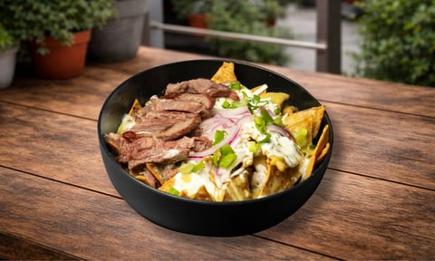 Bowl negro con carne asada y papas Rostizadas con cebollín sobre mesa de madera