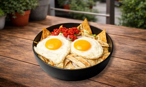 Bowl negro con dos huevos fritos, totopos y salsa roja sobre mesa de madera en patio exterior