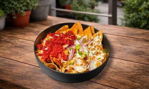 Bowl negro con nachos cargados con queso, salsa roja y toppings sobre mesa de madera